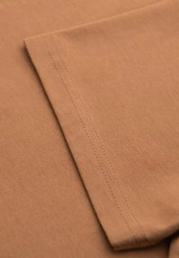 Hn�ědá bavlněná tkanina s hladkou texturou, se skládacím rukávem a pečlivým šitím, které zdůrazňuje minimalistický a jednoduchý design.