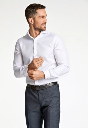 Weißes Langarmhemd mit klassischem Kragen, kombiniert mit dunkelgrauen Hose und einem schwarzen Gürtel, mit einer glatten Stoffoberfläche.