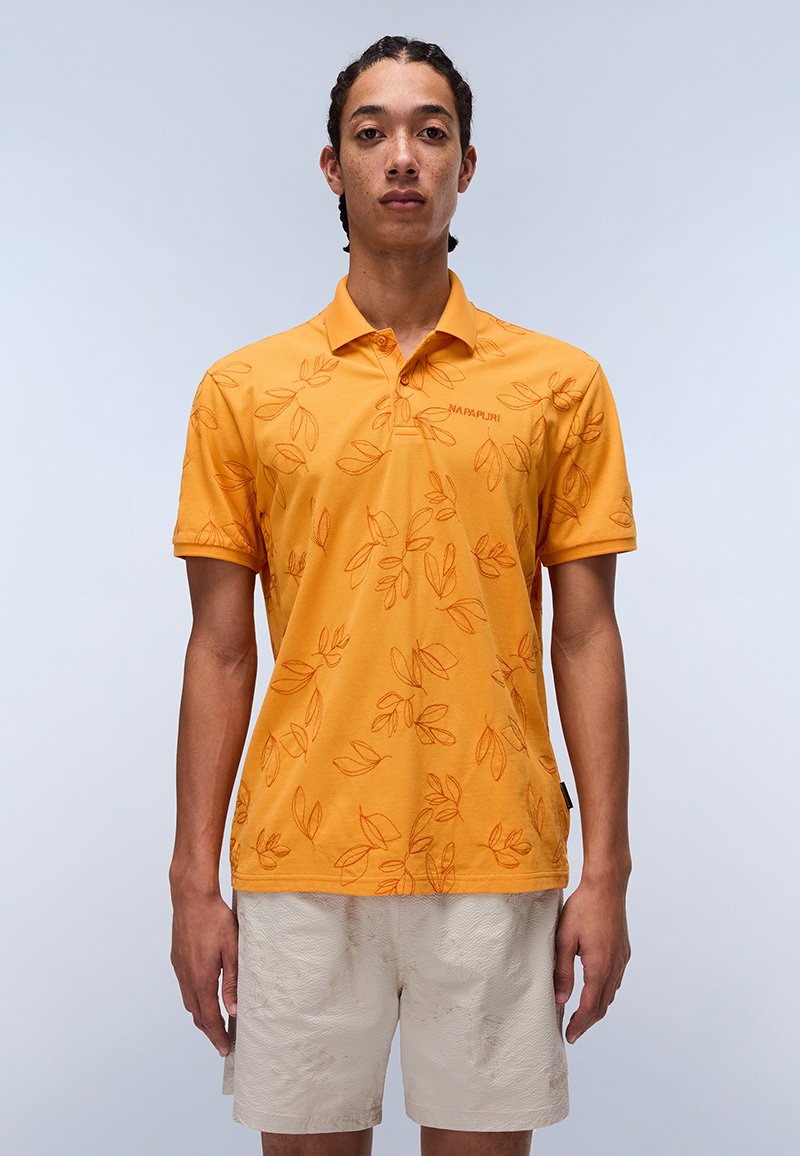 Gul polo trøje med bladmønster i en lysere nuance, korte ærmer og krave. Båret med lyse shorts.