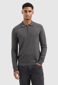 Langærmelige polo in donkergrijze stof met een ritskraag en geribde manchetten, gecombineerd met donkere jeans. Met een gladde textuur en een aansluitend ontwerp.