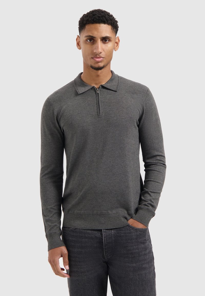 Langærmelige polo in donkergrijze stof met een ritskraag en geribde manchetten, gecombineerd met donkere jeans. Met een gladde textuur en een aansluitend ontwerp.