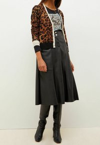 Leopardmönstrad cardigan med svarta accenter, parat med en höga midjan svart läderskjorta. Svarta ankelstövlar fulländar outfiten.