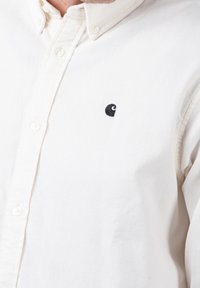 Witte corduroy shirt met een button-down kraag, voorzien van een klein zwart logo op de linkerkant van de borst. Textiel met verticale ribben.