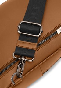 Brown leather bag featuring a black fabric strap with embossed lettering, metallic hardware, and a visible zipper detail.