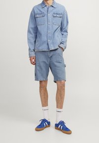 Light blue denim jacket with two chest pockets, paired with matching blue denim shorts. Worn with blue sneakers and white socks.