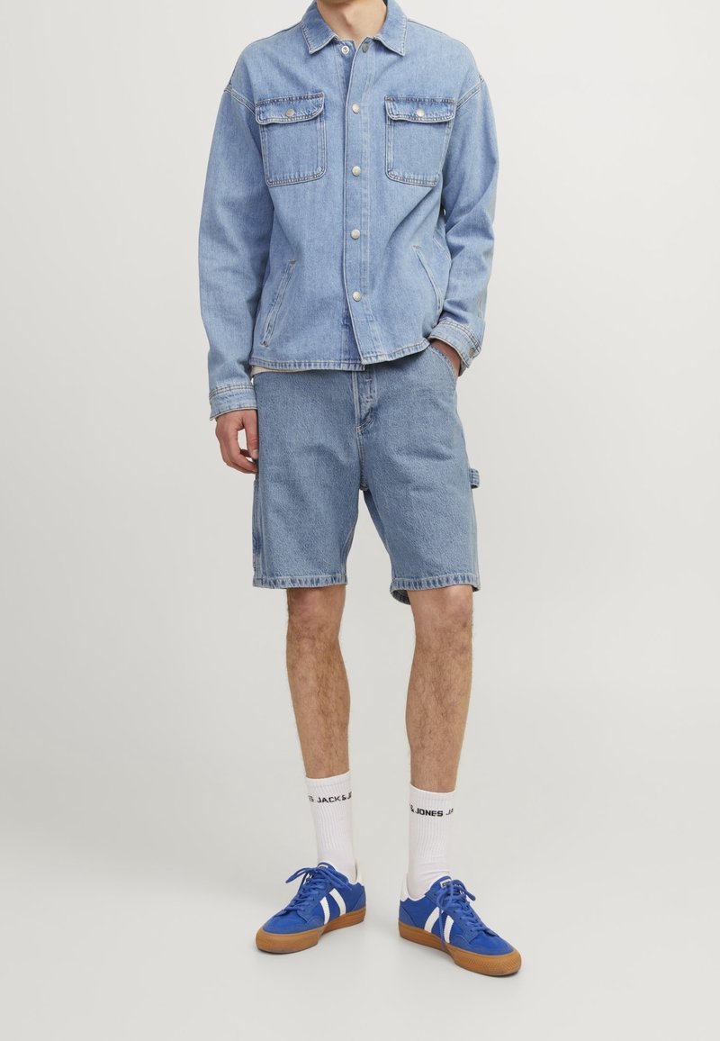Light blue denim jacket with two chest pockets, paired with matching blue denim shorts. Worn with blue sneakers and white socks.