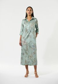 Langes, hellblaues Blumenkleid aus Satin, mit kentkragen und Dreiviertelärmeln, Taschen und einer fließenden Silhouette.