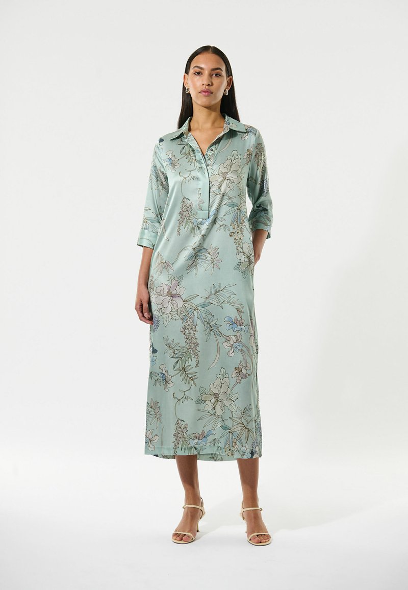 Langes, hellblaues Blumenkleid aus Satin, mit kentkragen und Dreiviertelärmeln, Taschen und einer fließenden Silhouette.