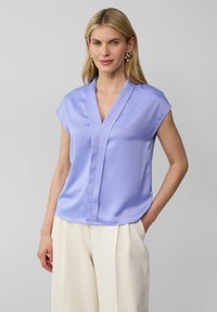 Lichtpaarse blouse met korte mouwen en een V-hals, met een gladde textuur en subtiele voorschijnnaden, gecombineerd met crèmekleurige broeken.