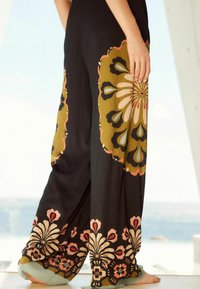 Pantalon à jambes larges en tissu noir avec des motifs floraux en olive, rose et bleu. Détails remarquables : finition texturée et ourlets bordés.