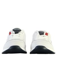 Baskets de sport blanches avec une tige en cuir lisse, semelle en caoutchouc noire et fermeture à lacets ; présentent un accent rouge près des lacets.