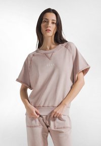 Felpa rosa chiaro con vestibilità morbida, maniche corte e polsini a costine. Presenta un logo discreto al centro e dettagli di cuciture a contrasto.