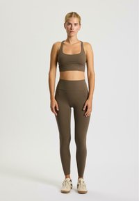 Bruine sport-bh en high-waisted legging, gemaakt van rekbaar materiaal. Gladde textuur, minimale naden, met schoenen in neutrale tinten.