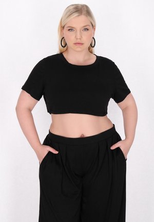 Sort crop top med korte ærmer og rund halsudskæring, parret med løstsiddende sorte bukser med sidelommer og en glat overflade.