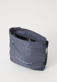 Borsa a tracolla in nylon grigio con zip sulla parte superiore, con una stampa del logo e una texture liscia. Cinghia regolabile per un trasporto versatile.