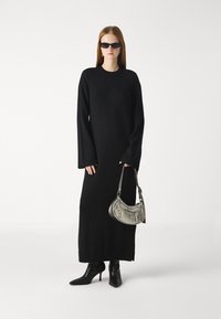 Melnas, garās piedurknes adīta kleita ar platu piedurkņu modeli, saskaņota ar melnām, norādītām augstpapēžu zābakām un mazu metalizētu sudraba rokassomu.