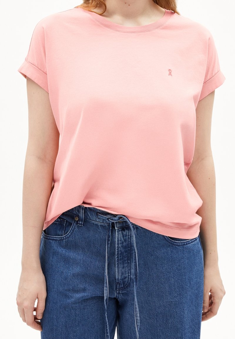 Ljusrosa bomullströja med rullade ärmar, rund hals och liten broderad logotyp. Vänligt ihop med mörkblå denimjeans med dragsko.