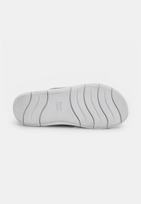 Talpa de sneaker albă cu un grip texturat, având caneluri de flexibilitate proeminente și branding. Material din cauciuc neted cu accente minime.