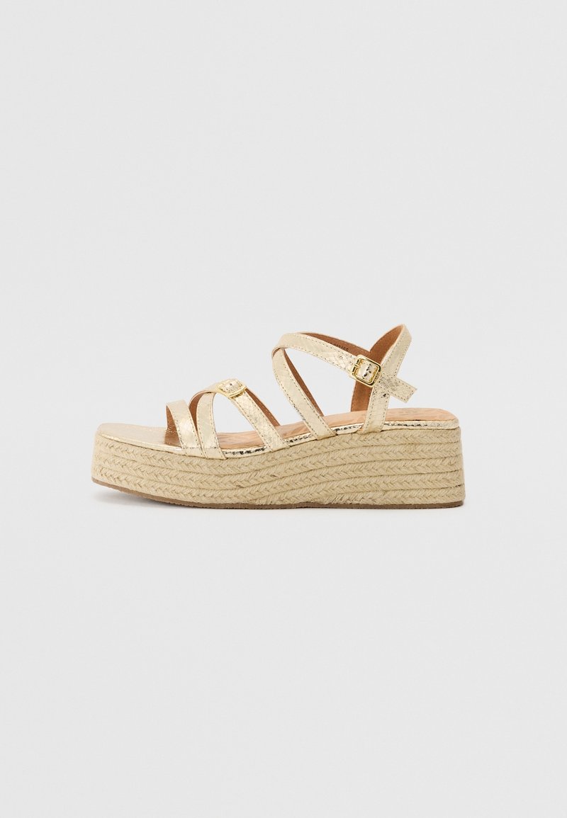 Sandales à plateforme métalliques dorées avec des brides croisées, semelle en jute tressé et détail boucle. Texture lisse avec une légère brillance.