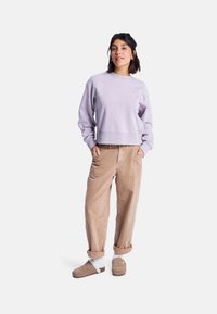 Felpa lilla corta con scollo rotondo, abbinata a pantaloni in corduroy beige e pantofole marroni con dettagli bianchi.