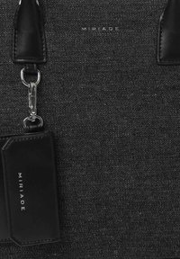 Borsa tote in denim nero con dettagli in pelle, dotata di una catena in metallo argentato e un portacarte removibile. Logo del marchio "MIRIAD" stampato in modo prominente.
