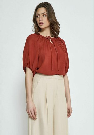 Rust-colored blouse with a textured fabric, gathered neckline, and tie detail. Features short, puffed sleeves and a relaxed fit.