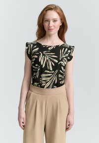Top nero con motivo a foglia in beige e verde, dotato di maniche corte a campana, abbinato a pantaloni beige a vita alta.
