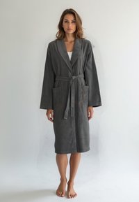 Accappatoio in spugna grigia con maniche lunghe, cintura e due tasche frontali. Texture morbida e design fino al ginocchio.