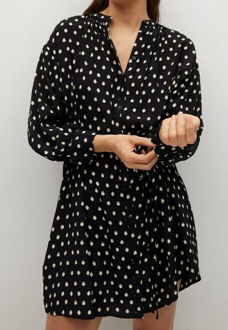 Femme ajustant le poignet d'une robe noire à manches longues avec des pois blancs et une patte de boutonnage devant.