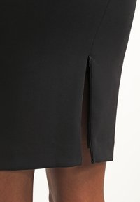 Close-up of black skirt with side slit featuring a small zipper, worn by a person with medium brown skin.