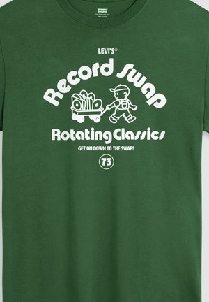 Groen T-shirt met witte tekst "Record Swap Rotating Classics" en een illustratie van een persoon die een kar met vinylplaten trekt.