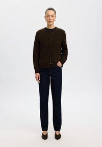 Rjav pleteni kardigan s okroglim ovratnikom in sprednjim zapenjanjem na gumb, v kombinaciji z temno modrimi kavbojkami in črnimi čevlji s peto. Gladka tekstura.