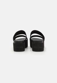 Black platform sandals with wide straps, featuring a smooth texture and a branded heel. The design offers an elegant and modern silhouette.