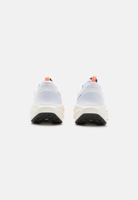 Hvite sportssko med mesh-overdel, polstret krage og oransje detaljer på hælen, med en teksturert svart gummisåle.