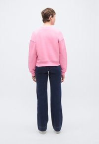 Ροζ φούτερ με ριμπ μανσέτες και τελείωμα, σε συνδυασμό με σκούρο μπλε καμπάνες τζιν. Το σύνολο έχει χαλαρή εφαρμογή και εμφανείς ραφές.