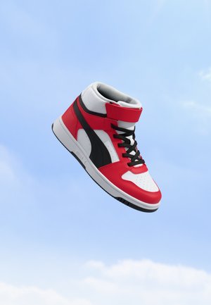 Baskets montantes avec des panneaux rouges, blancs et noirs et des lacets noirs flottant sur un fond de ciel bleu clair.