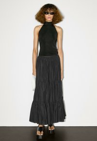 Top nero a fascia abbinato a una gonna maxi nera a strati. L'outfit presenta un tessuto testurizzato e sandali neri piatti con plateau.