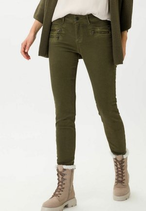 Pantalons en coton vert olive ajustés avec poches zippées à l'avant, associés à des bottes marron clair avec doublure en polaire blanche et détail de lacets.