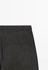 Gros plan sur le dos d'un pantalon en tissu gris foncé avec poche passepoilée simple et couture de la ceinture sur fond blanc uni.