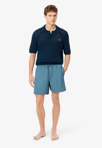 Polo a maglia navy con maniche corte e colletto, abbinato a pantaloni da mare azzurri chiari con vita elastica. Look complessivo casual.