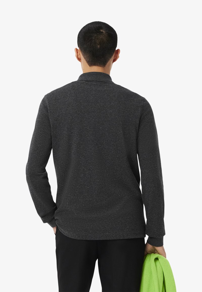 Polo shirt à manches longues gris foncé, texture douce, avec col et patte de boutonnage. Présente une coupe ajustée et un ourlet arrondi, porté avec un accessoire vert.