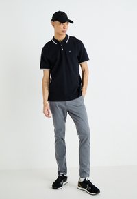 Μαύρο πόλο μπλουζάκι με λευκές λεπτομέρειες, γκρίζες παντελόνες και μαύρα αθλητικά παπούτσια. Χαλαρή εμφάνιση, με απλό σχέδιο και αναπνεύσιμο ύφασμα.