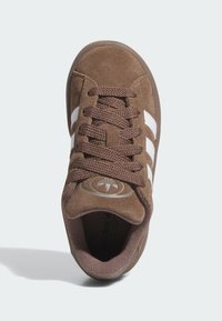 Brown suede sneaker with white stripes, round toe, textured surface, and lace-up closure; features a circular logo on the tongue.