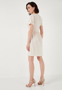 Short-sleeve cream dress with a fitted bodice and flared skirt, made of lightweight fabric; paired with beige high-heeled sandals.