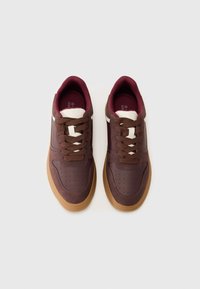 Brown sneakers with a smooth texture, maroon accents, white stripes, and perforated upper design. Features round laces and a gum sole.