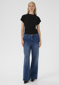 Čierny top s krátkym rukávom v kombinácii so širokými modrými džínsami. Džínsovina má vysoký pás, jemné vyblednutie a klasický dizajn s piatimi vreckami.