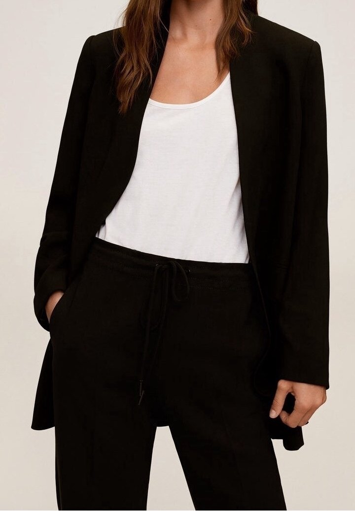 Sort blazer over en hvid tanktop, parret med sorte bukser med snøre. Har en skræddersyet pasform og glat tekstur.