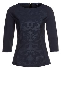 Marinblus med trekvartslånga ärmar, texturerad yta med en subtil damaskmönster, rundad halsringning och bakre dragkedjedetalj.