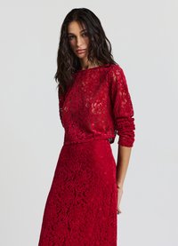 Abito di pizzo rosso con maniche lunghe, texture trasparente, vita aderente e intricate fantasie floreali. Progettato per una silhouette aderente.
