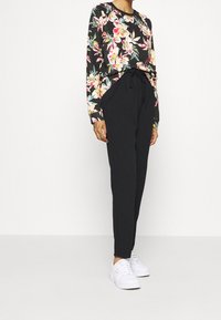 Sudadera negra con flores y mangas largas, que presenta un vibrante patrón floral. Combinada con pantalones joggers negros y zapatillas blancas.
